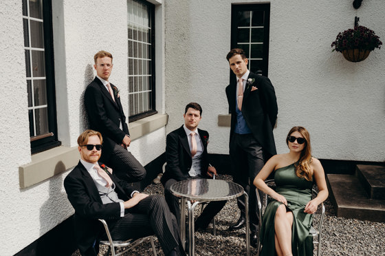 Groomsmen and bridesmaid relax at table outdoors
